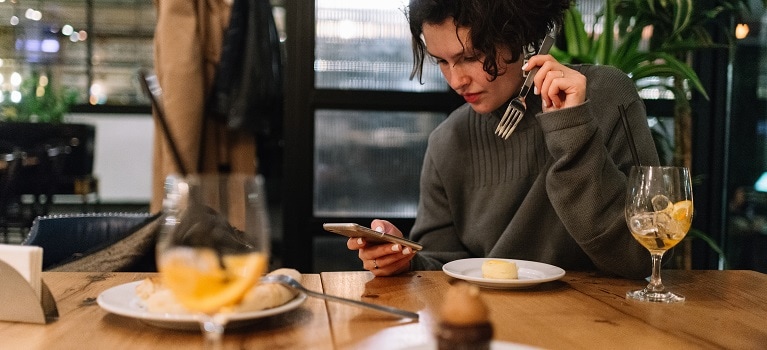 person looking at phone while eating dinner