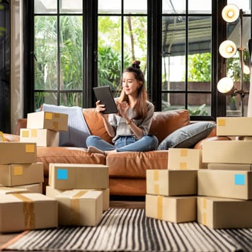 A person surrounded by boxes and looking at a tablet