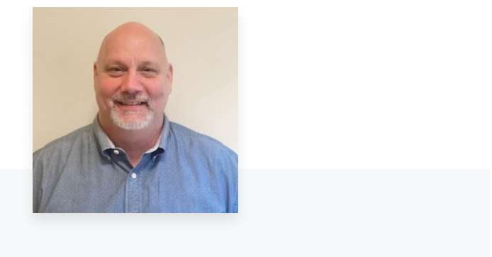 Man in grey dress shirt smiling at camera
