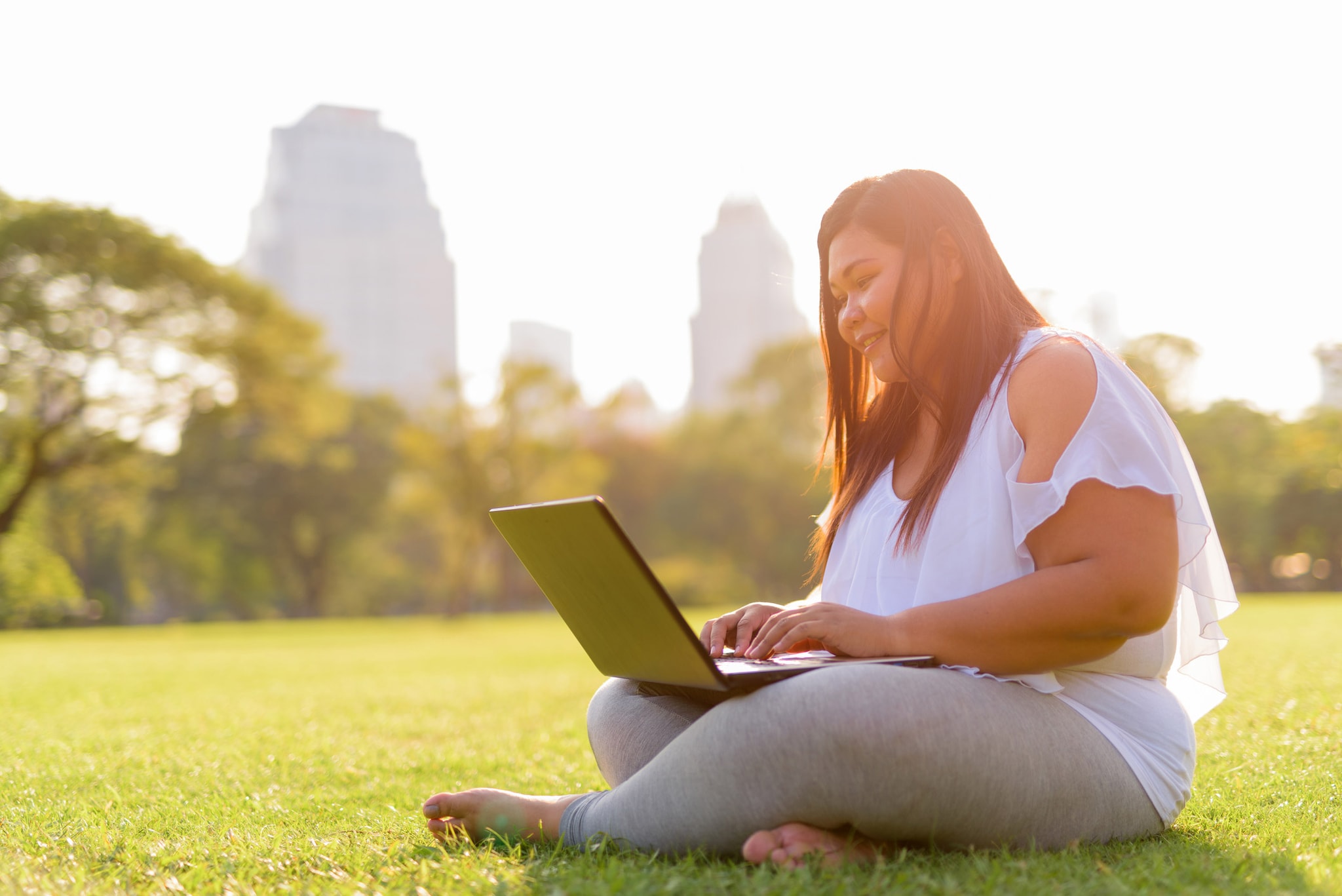 A woman sits in a park while using her laptop