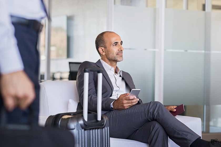 Man is sitting in the chair in the airport and holding the cellphone