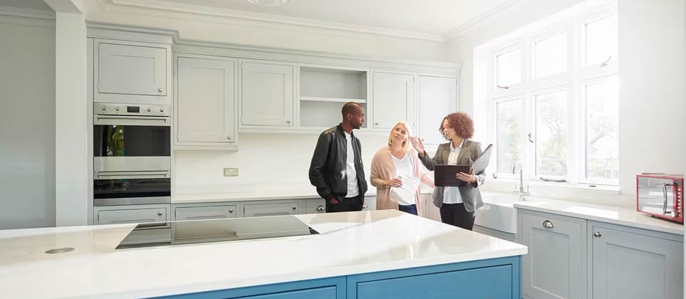 How Much Should You Save Each Month? A real estate agent explaining modern kitchen features to a couple.