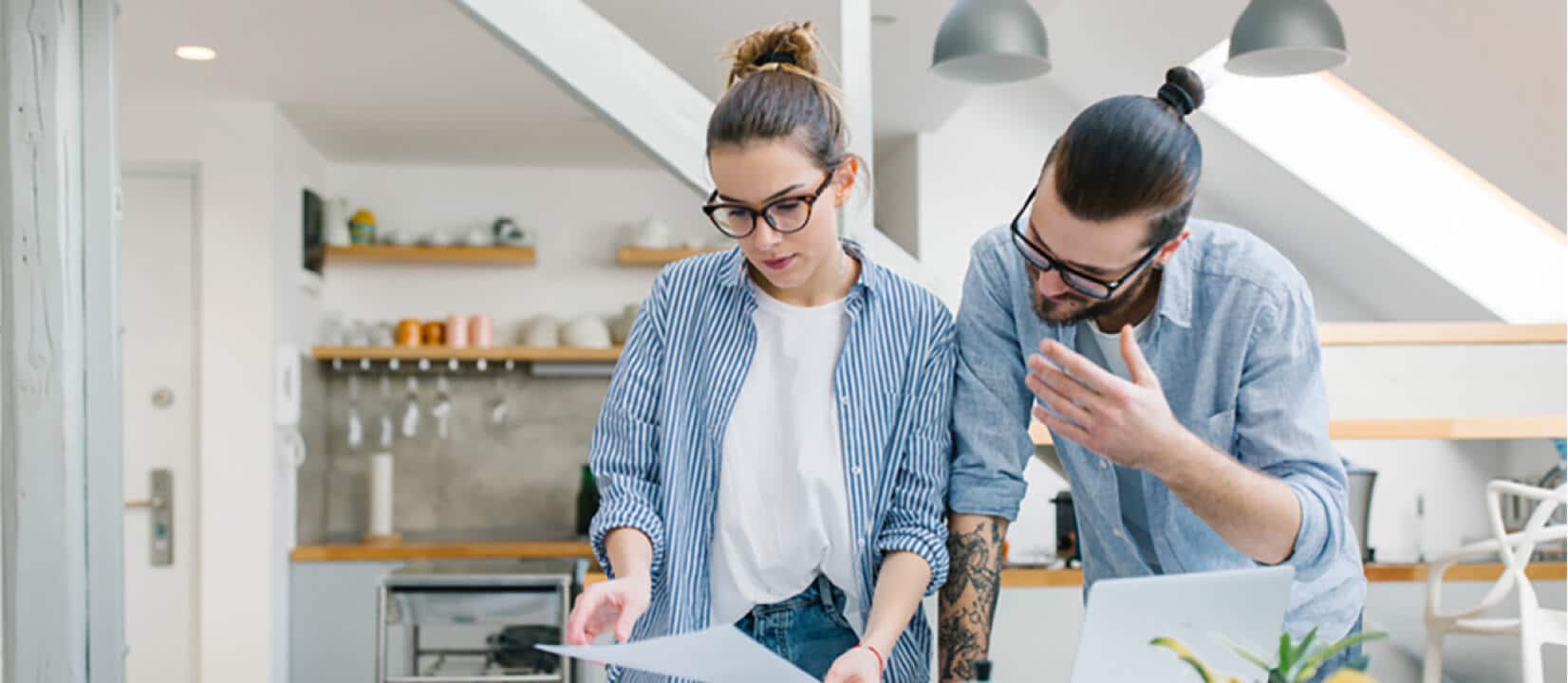 A man and a woman standing over a dining room table while looking over some papers A man and a woman standing over a dining room table while looking over some papers