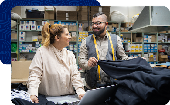 Two smiling business owners working in a textile factory and reviewing their rewards on a laptop.