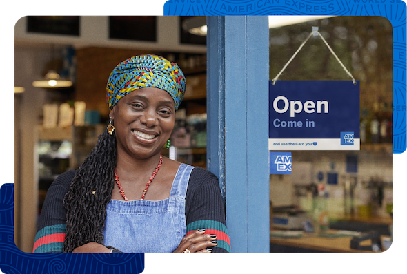A smiling business owner standing next to a sign that says “Open. Come in and use the Card you love. American Express”