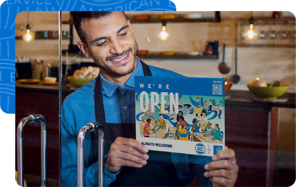 Store owner holding a sign saying “We’re Open. Always Welcome”