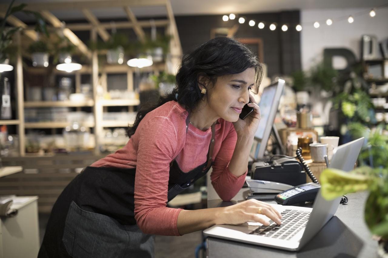 Small business woman in shop on the phone and looking at laptop