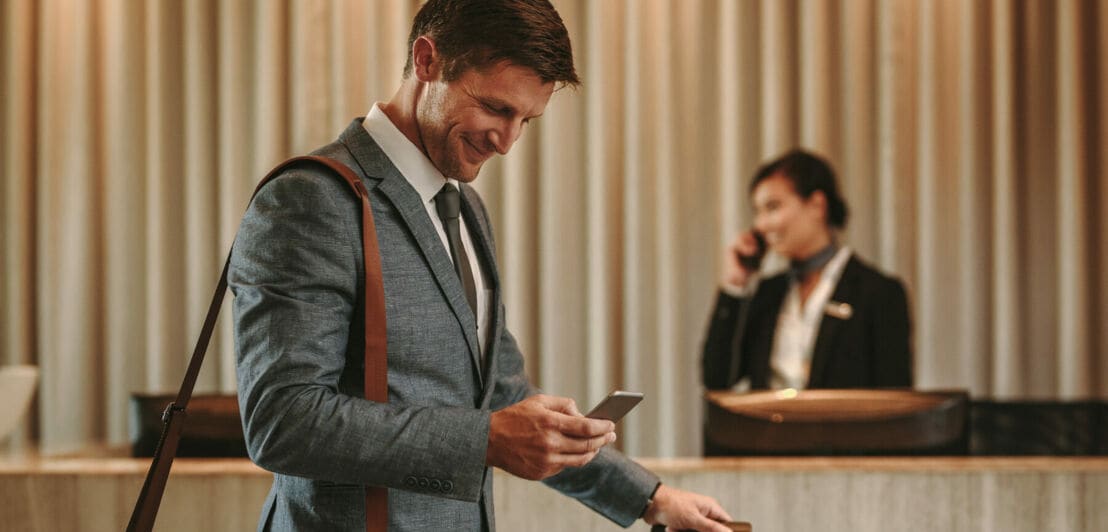 Ein Geschäftsmann schaut lächelnd auf sein Smartphone in einer Hotellobby Ein Geschäftsmann schaut lächelnd auf sein Smartphone in einer Hotellobby